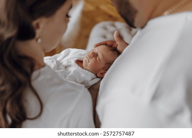 A couple is holding a baby in their arms. The baby is sleeping and the parents are looking at it