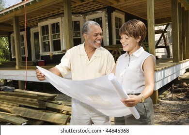 Couple holding blueprints on construction site.  Horizontally framed shot.