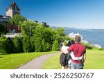 a couple holding each other in a park overlooking the old area of quebec city canada on a sunny day.