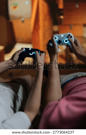 Couple holding glowing wireless controllers, immersed in virtual reality gaming on large screen at home, sharing high-tech entertainment, connection, and relaxed leisure together.