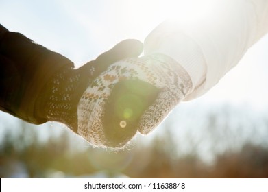 Couple holding hands in gloves in winter season at sunlight