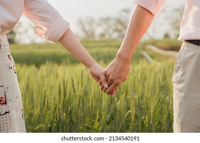 couple holding hands in a green field at sunset - Powered by Shutterstock