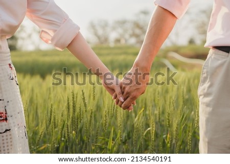 couple holding hands in a green field at sunset