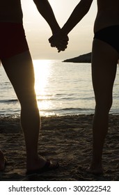Couple holding hands on a beach at sunset, silhouette effect.