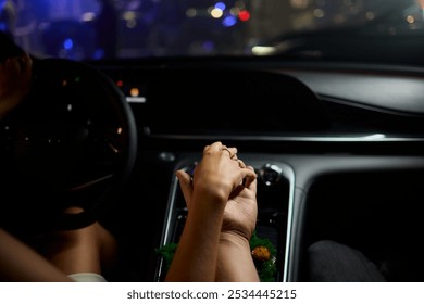 A couple holding hands in their car, embracing intimacy while driving through the city at night - Powered by Shutterstock