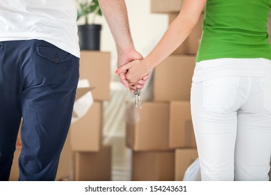 Couple Holding Hands Together In New Home, Lot Of Cardboard Boxes In Background 