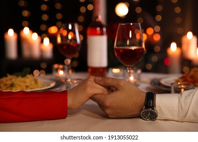 Couple holding hands together at table during romantic dinner in restaurant, closeup