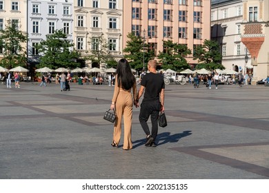 A Couple Holding Hands Walking Through The Old Town Outdoors On A Sunny Summer Day Towards Horse-drawn Carriages And A Summer Restaurant In The Background, A Couple Of Tourists, Adult Couple