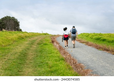 Couple holding hands and walking uphill under a cloudy sky. Long Bay Coastal Okura Track. Auckland. - Powered by Shutterstock