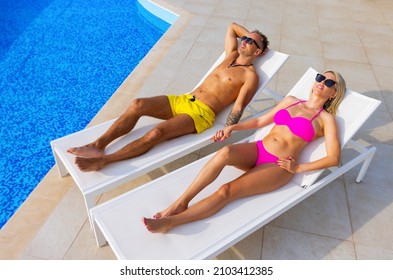 Couple holding hands while sunbathing by the pool