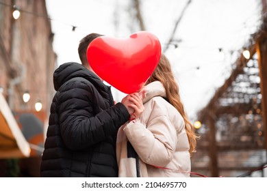 Couple holding a heart-shaped balloon and kissing on the street. Valentine's day concept, gifts, love