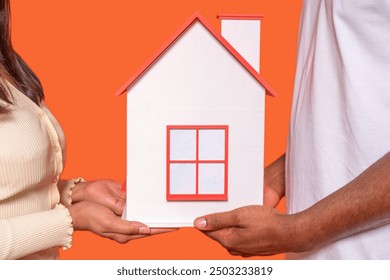 Couple Holding Miniature House Model Against Vibrant Orange Background - Powered by Shutterstock