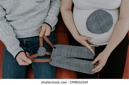 
Couple Holding Newborn Baby's Things While Sitting On Sofa, Top View Close-up.