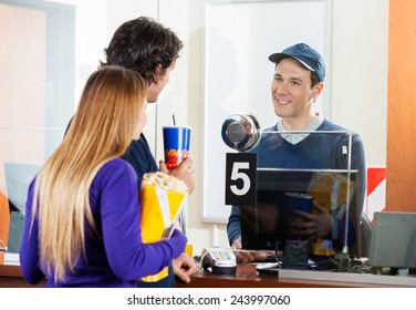 Couple Holding Popcorn And Drink While Buying Movie Tickets At Box Office