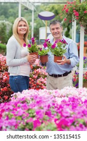 Couple Holding Purple Plants In Garden Centre And Smiling