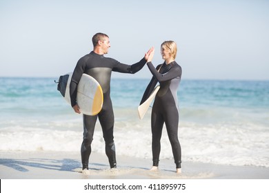 Couple holding a surfboard and giving a high five to each other on the beach - Powered by Shutterstock