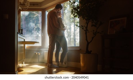 Couple At Home: Woman Watching Out Of Window Male Partner Embraces Her From Behind. Happy Couple In Ideal Relationship Spending Sunny Day Together. Beautiful Family Moments