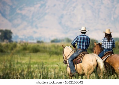 a couple horseback riding from behind overlooking wide open field and mountains of Utah wilderness