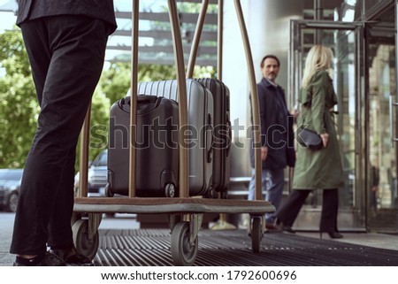 Couple of hotel guests entering a hotel while looking back at a porter managining a trolley with their suitcases Сток-фото © 