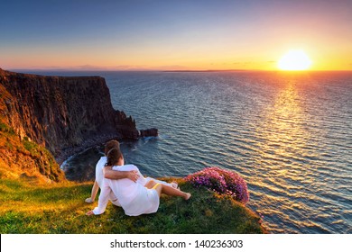 Couple in hug watching sunset on the edge of the cliff.