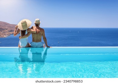 A couple hugging at the edge of an infinity pool and enjoying the view to the blue, mediterranean sea during summer vacation time