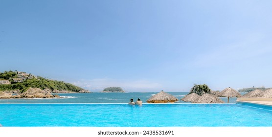 A couple hugging at the edge of an infinity pool and enjoying the view to the blue of Tangolunda Bay in Huatulco Oaxaca