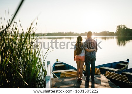 Couple hugging and looking in the sunset on pier. Back view.