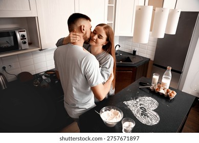 A couple hugs in the kitchen while preparing food. They enjoy their time together as they cook and connect in the warm setting of their home.