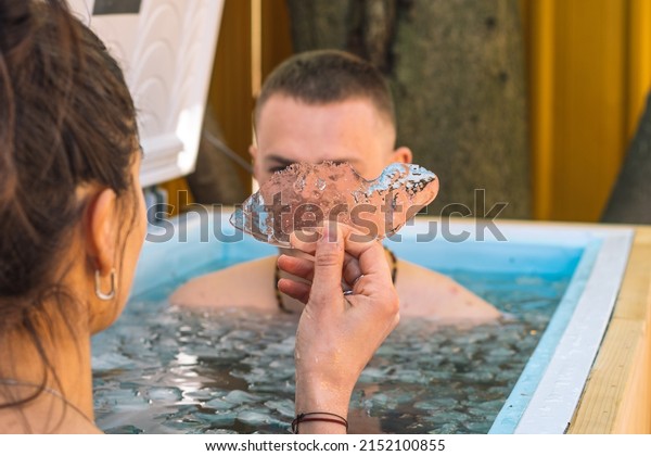 Couple\
ice bathing in the cold water among ice cubes with girl holding a\
piece of ice in her hand covering boy\'s face. Wim Hof Method, cold\
therapy, breathing techniques, yoga and\
meditation