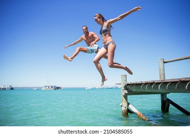 Couple jumping off wooden dock into water - Powered by Shutterstock