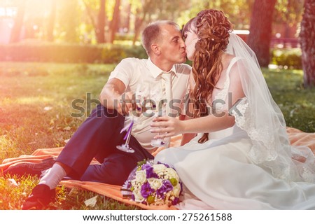 couple just married sitting in park green grass with bouquet of flowers and wine glasses.
