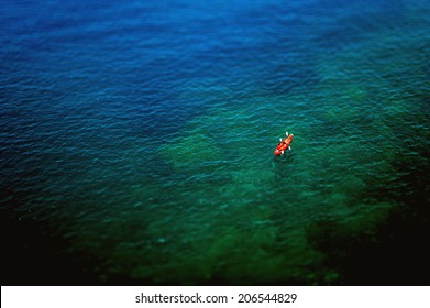 Couple Kayaking In Wide Blue Sea As Seen From Above. Tilt-shift Lens Used To Emphasize The Rowers