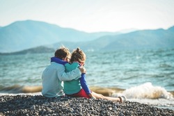 Couple Kids Hug Each Other On Sea Beach. Children Playing With Sand On Summer Beach. Happy Children Run At Sea Beach. Kids Are Playing Merrily. Boy And Girl Look On Beautiful Nature. Back View