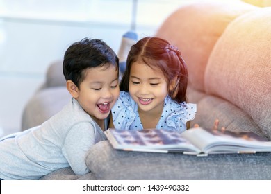 A couple kids reading book together in living room while sister is lying on sofa and brother sitting on floor. Having fun and excited or interested book stories with happiness smiling, laughing face 