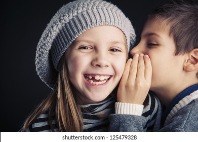 Couple Of Kids Whispering On Black Background.