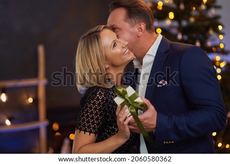 Couple kiss in front of chrismas tree holding gift. High quality photo