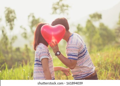 Couple Kissing Behind A Red Heart Balloons With Sunlight