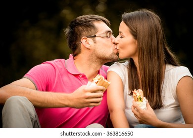 Couple Kissing And Eating Sandwich Outdoor On Date