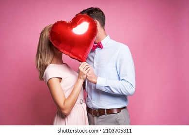 Couple kissing hidden behind one heart shape balloon - Shutterstock ID 2103705311