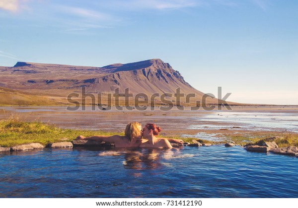 Couple kissing in natural hot bath with the\
spectacular Icelandic scenic view of the mountain and ocean coast,\
Westfjords Iceland