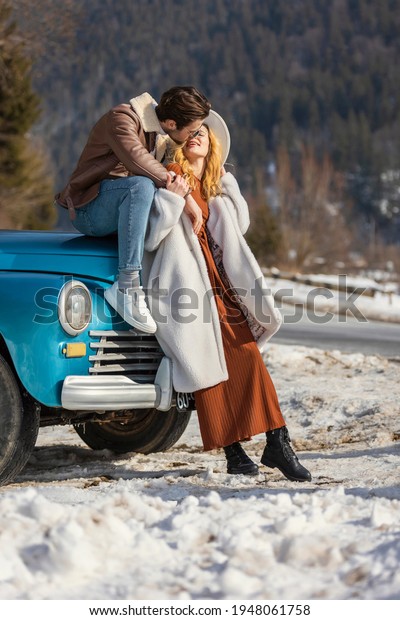 couple kissing near the car on the background of a\
snowy road