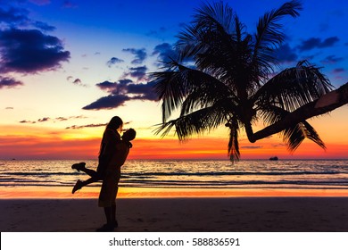 Couple kissing on the beach with a beautiful sunset in background, man lifting the woman on background sea ocean water and colorful sunset sky / Vacation couples in tropical paradise / Bali, Indonesia