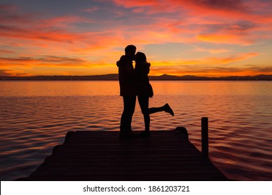 Couple Kissing On The Dock Of A Lake With A Red Sunset
