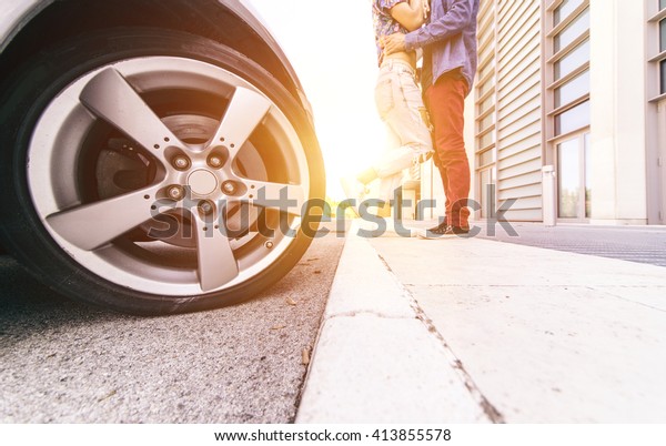 Couple\
kissing outside their car. Focus on the car\
wheel
