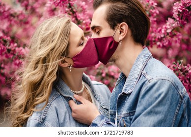 Couple kissing with protective face masks. Love during quarantine of coronavirus pandemic conception. Man and woman posing near spring blossom pink trees. Close up portrait
