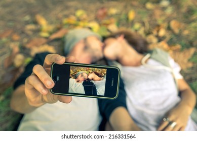 Couple kissing while taking a selfie with smart phone - autumn,people,love,technology,lifestyle concept