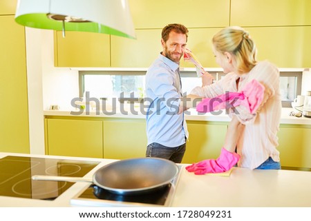 Couple in the kitchen argues playfully with cleaning rags because of housework