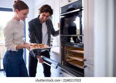 Couple In Kitchen At Home Putting Homemade Pizza Into Oven To Bake - Powered by Shutterstock