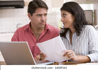 Couple In Kitchen With Paperwork Using Laptop Looking Unhappy