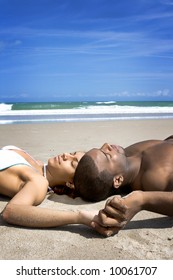 Couple laying on a beach. Blue sky in the background.